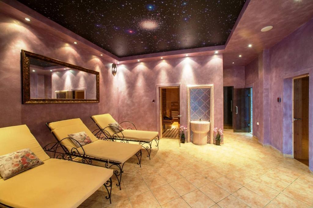 A spa relaxation room with three yellow lounge chairs, a large mirror, purple walls, a black starry ceiling, soft lighting, and open doors leading to a sauna and tiled shower area.