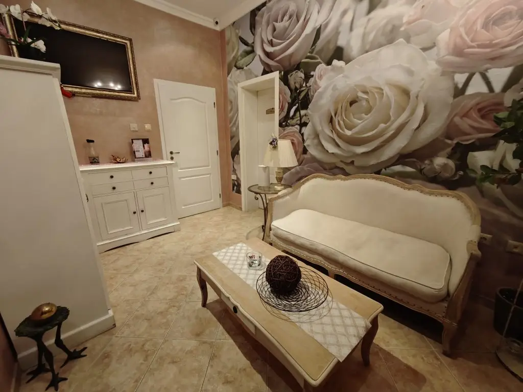 Elegant living room with cream-colored furniture, a floral mural featuring large roses on the wall, a coffee table with decorative items, a white cabinet, and a wall-mounted TV above the cabinet.