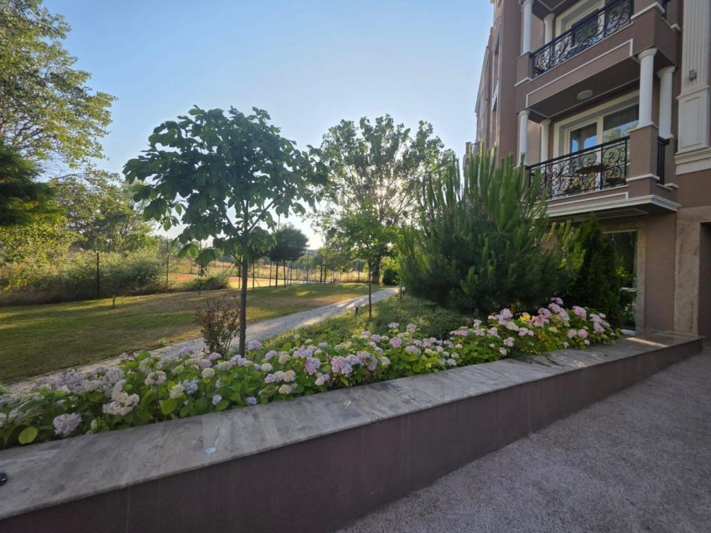 garden of flowering plants trees and green shrubs, beside a hotel building with balconies.