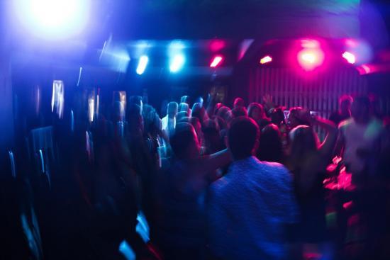 A blurry photo of people dancing in a crowded nightclub, illuminated by blue and pink lights with a vibrant, energetic atmosphere.